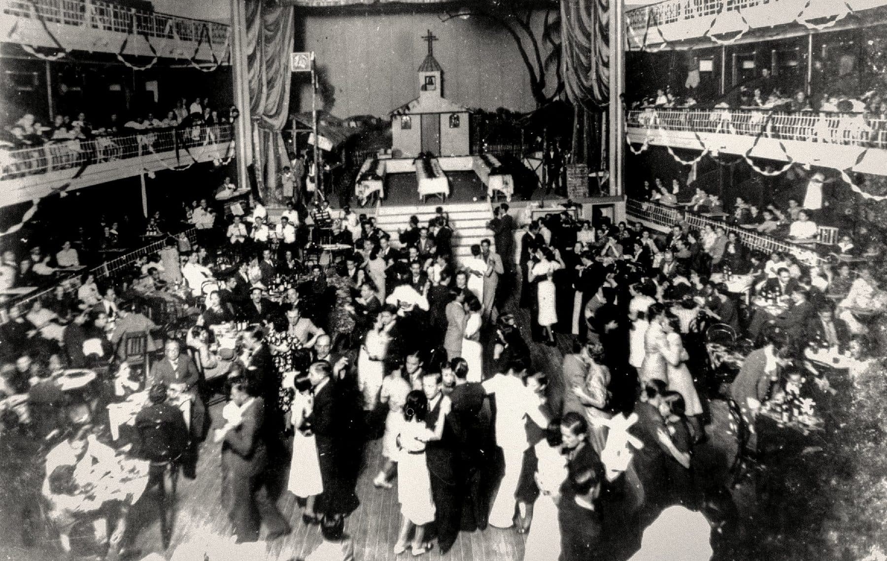 O interior em ferradura num baile histórico, com a plateia ocupada sob as galerias e os camarotes.